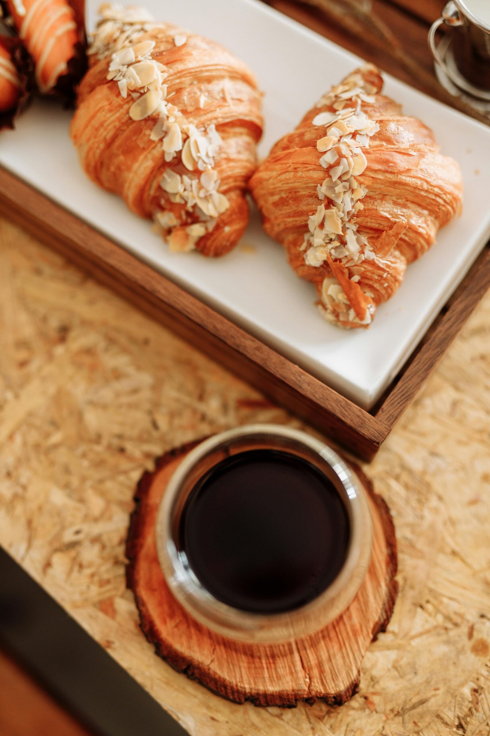 pexels-photo-6959943-6959943 Fresh almond croissants served with coffee on a rustic wooden table.